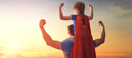 child sitting on top of parents shoulders flexing while looking at sunset