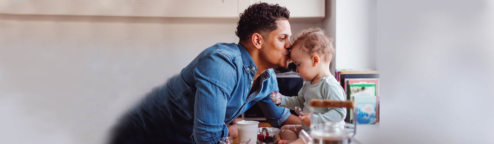 father kissing child's forehead in kitchen